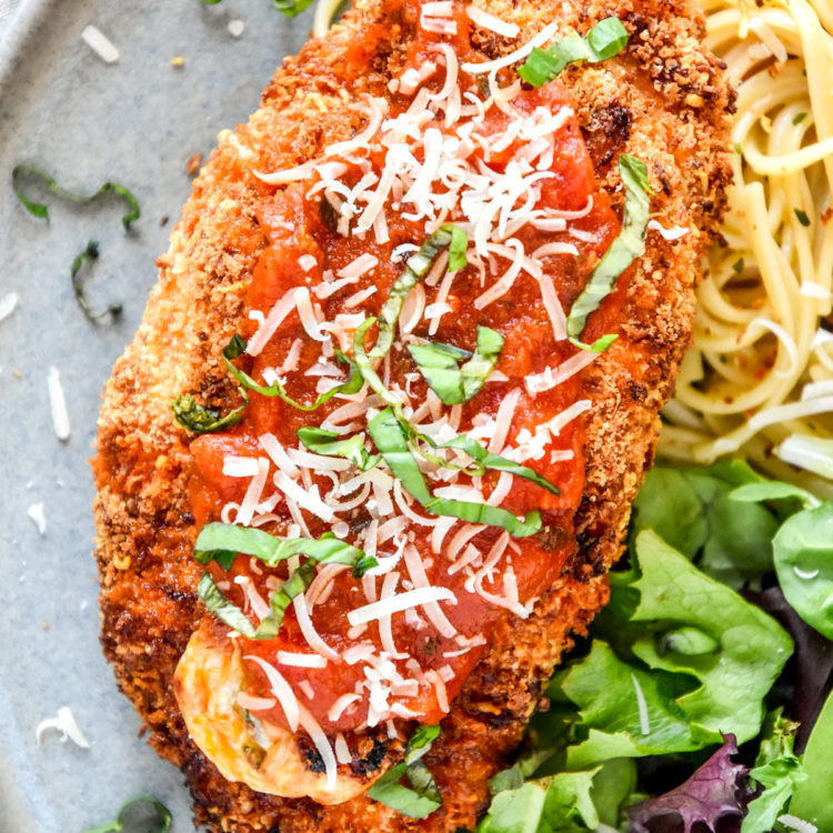 air fryer stuffed chicken parm on a plate with marinara spooned on top.