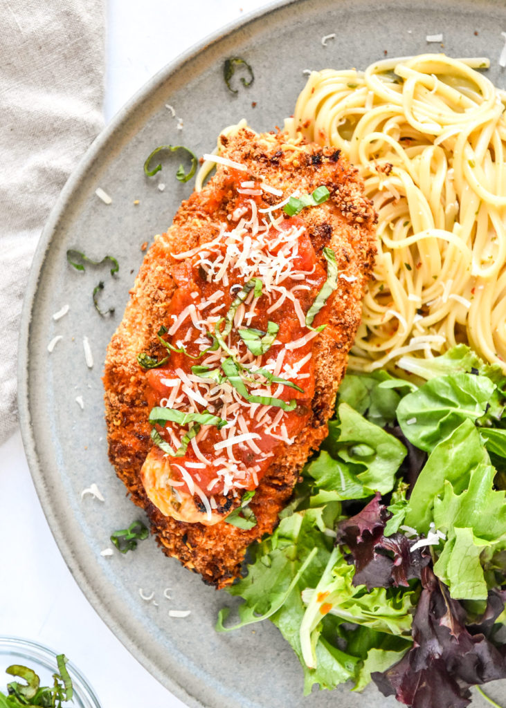 air fryer stuffed chicken parmesan on a plate with noodles and green salad.