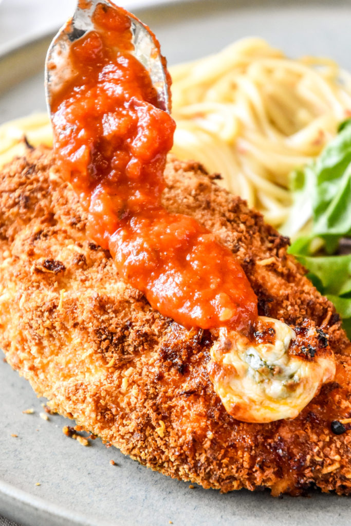 spooning marinara sauce on just cooked air fryer stuffed chicken parmesan.