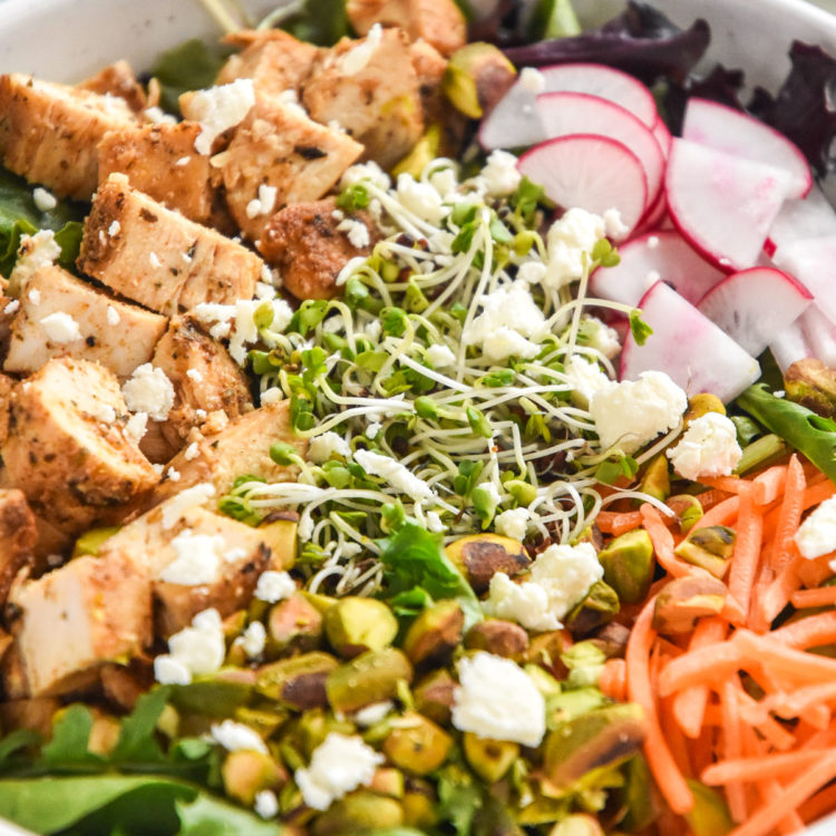 close up photo of simple spring mix lunch salad with chicken, carrots, pistachios, feta cheese, microgreens and more.