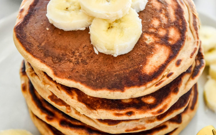 banana protein pancakes stacked on a plate with sliced bananas on top.