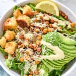 roasted chickpea caesar salad with avocado and croutons in a white bowl.