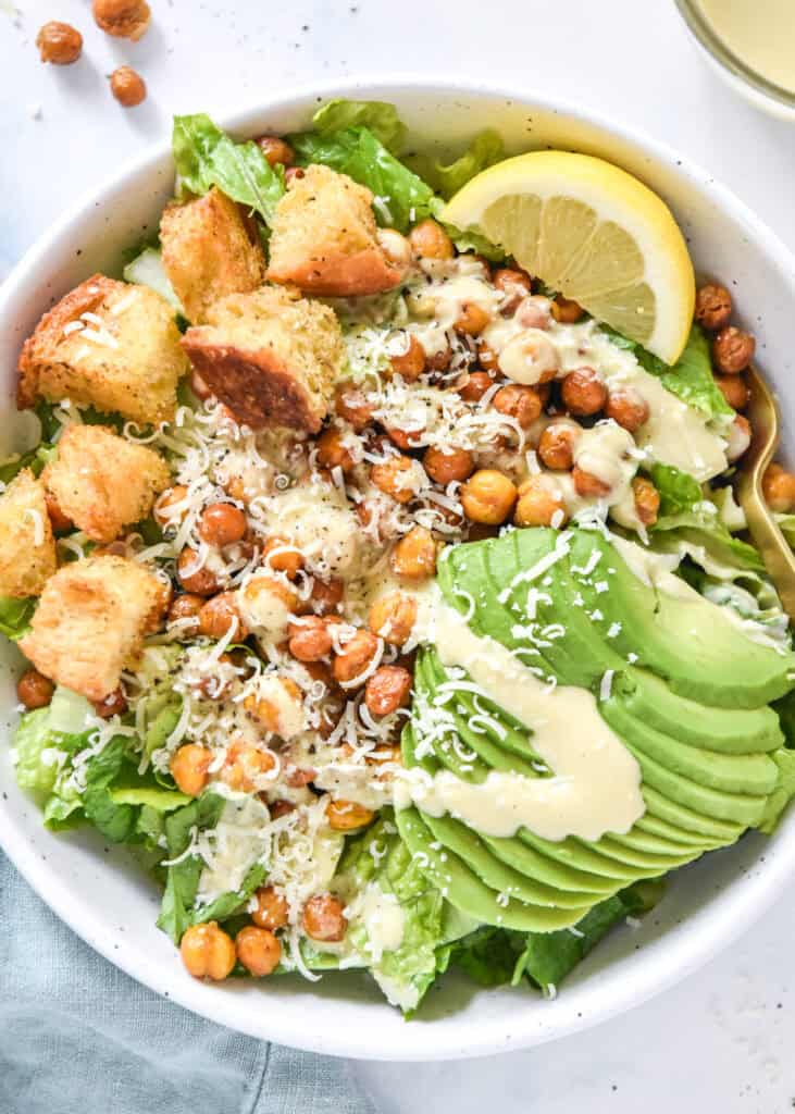 roasted chickpea caesar salad with avocado and croutons in a white bowl.