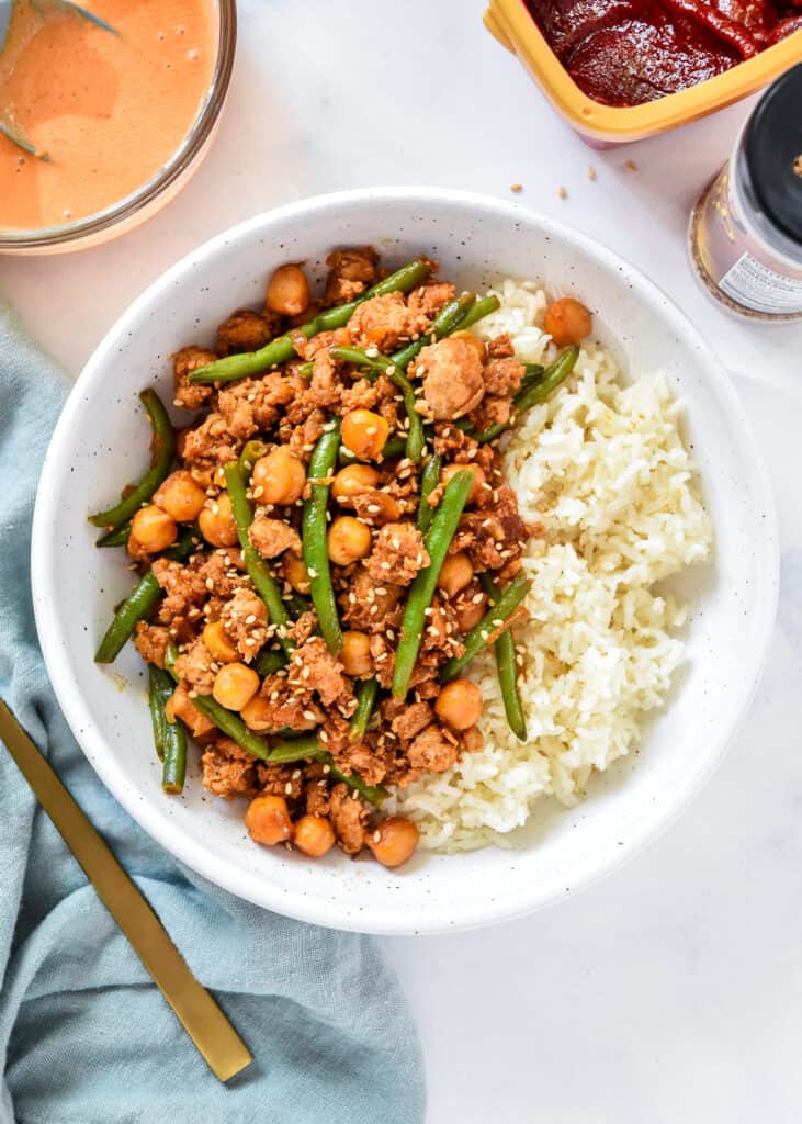 Korean-Inspired Gochujang Meat And Beans in a white bowl with rice and a fork.