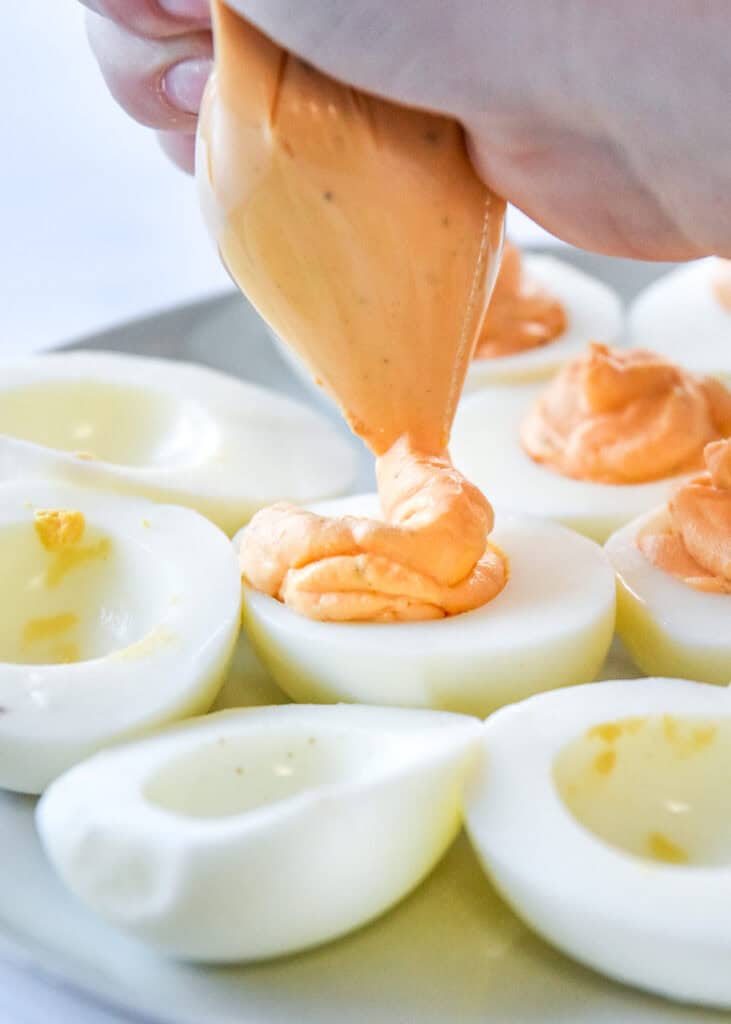 piping egg yolk mixture into the egg white shells to make deviled eggs.