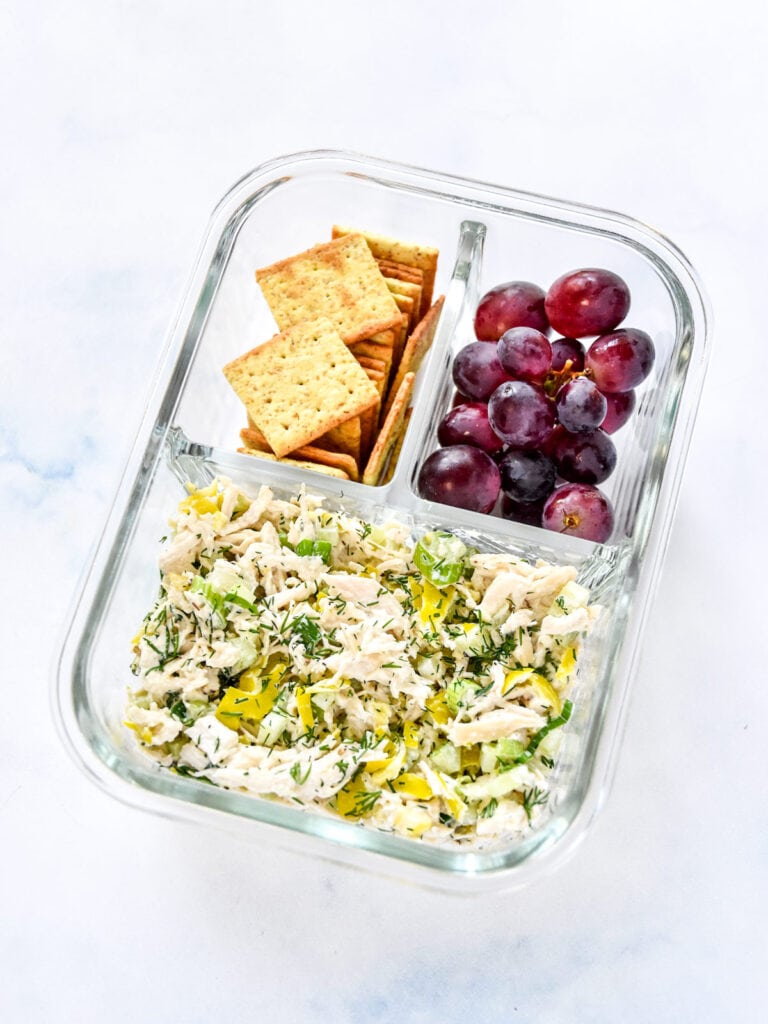 zesty pepperoncini chicken salad with crackers and grapes in a glass meal prep container.