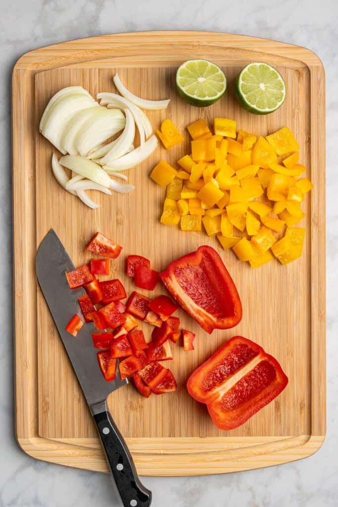 chopping peppers and onions on a wooden cutting board.