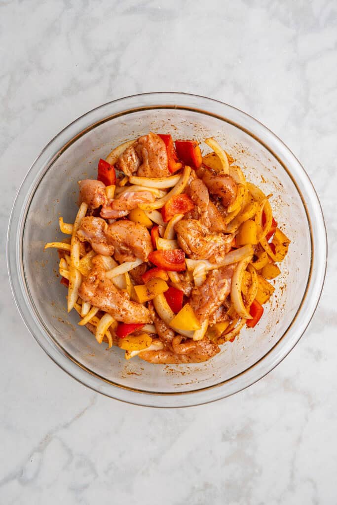 raw chicken and veggies covered in spice mix for the air fryer chicken fajitas.