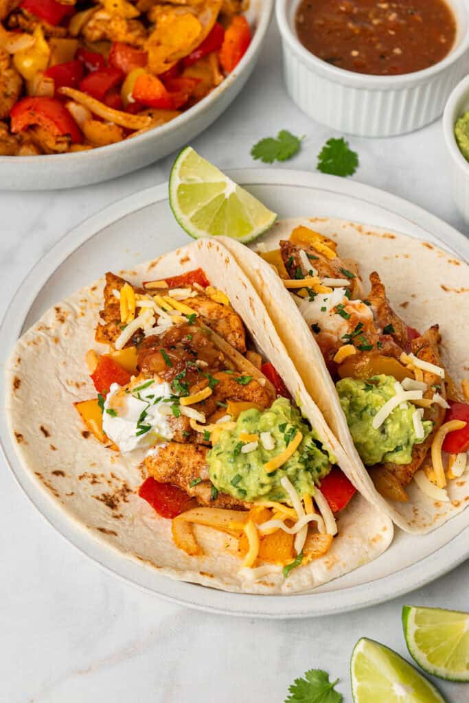 air fryer chicken fajitas on flour tortillas with shredded cheese, lime and avocado.