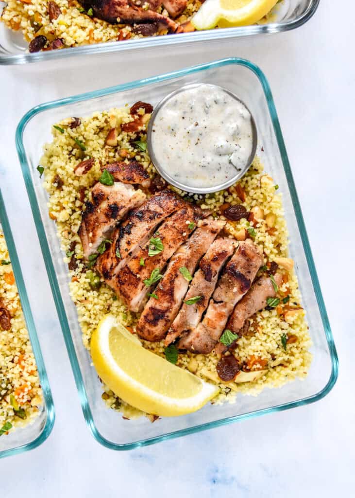 moroccan inspired spiced chicken couscous bowls with yogurt sauce and lemon wedge.