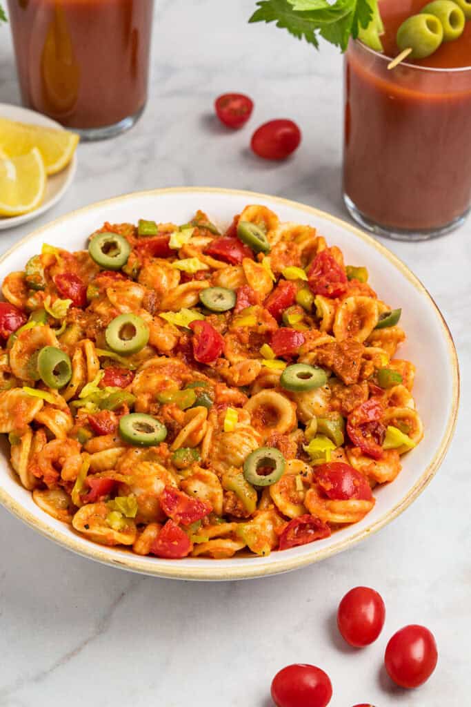 loaded bloody mary pasta salad in a white bowl with green olives on top.