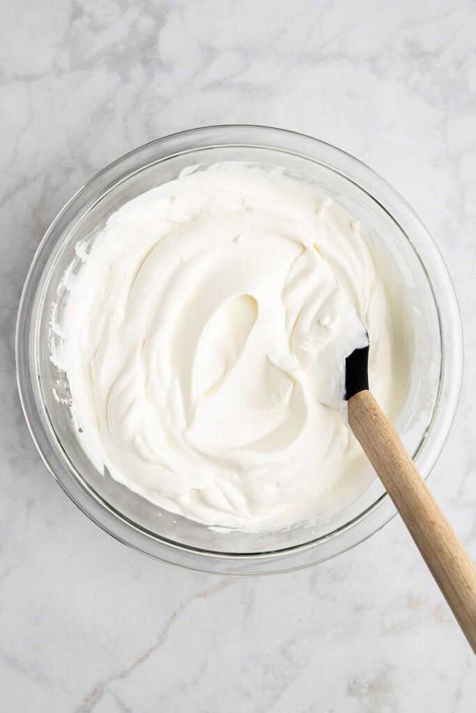 whipped cream in a glass bowl with rubber spatula.