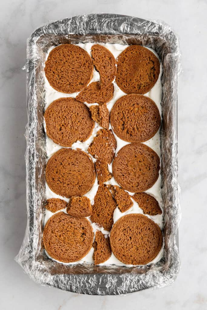 a layer of broken gingersnap cookies on top of whipped cream in a loaf pan.