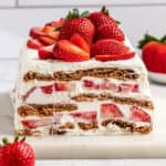 strawberry gingersnap icebox cake with fresh strawberries on top, sliced to see the interior.