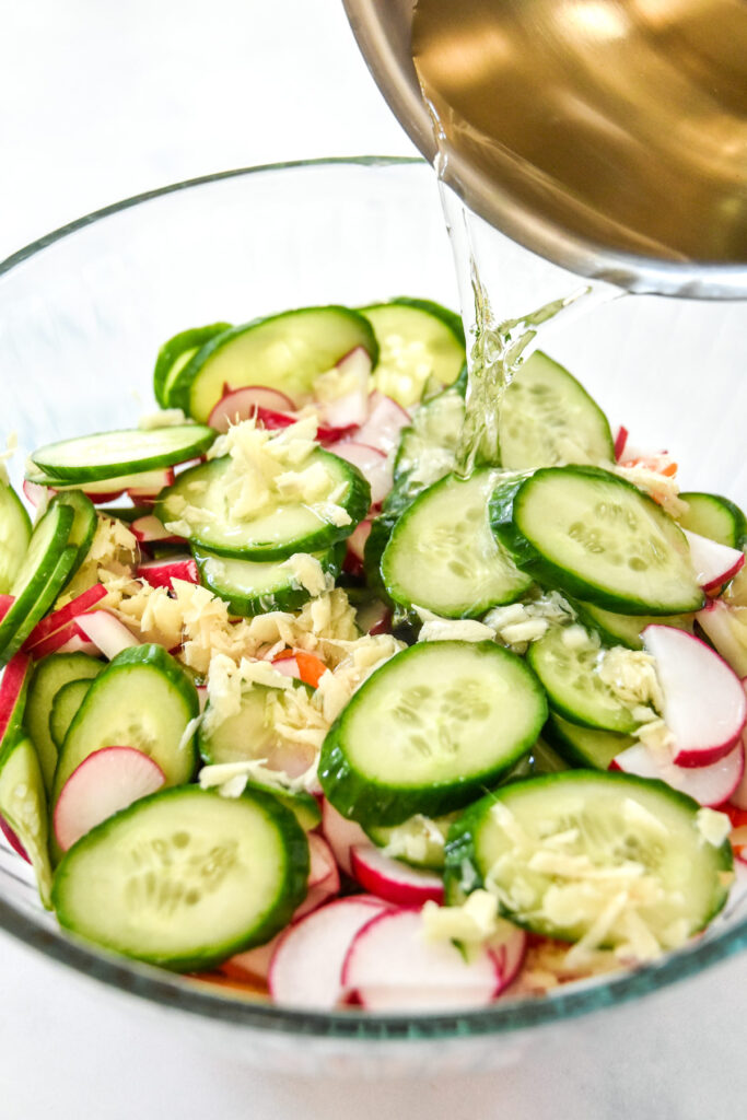 pouring pickling liquid into a bowl of sliced cucumbers carrots and radish.