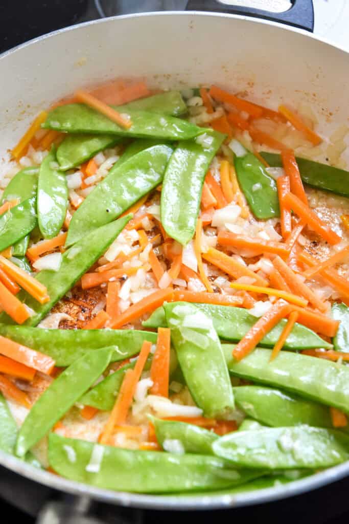 peas carrots and onions in a pan cooking on the stovetop.