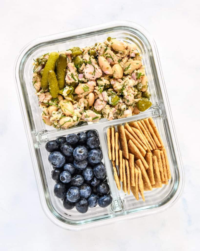 French-Style Tuna White Bean Salad in a glass meal prep container with blueberries and crackers.