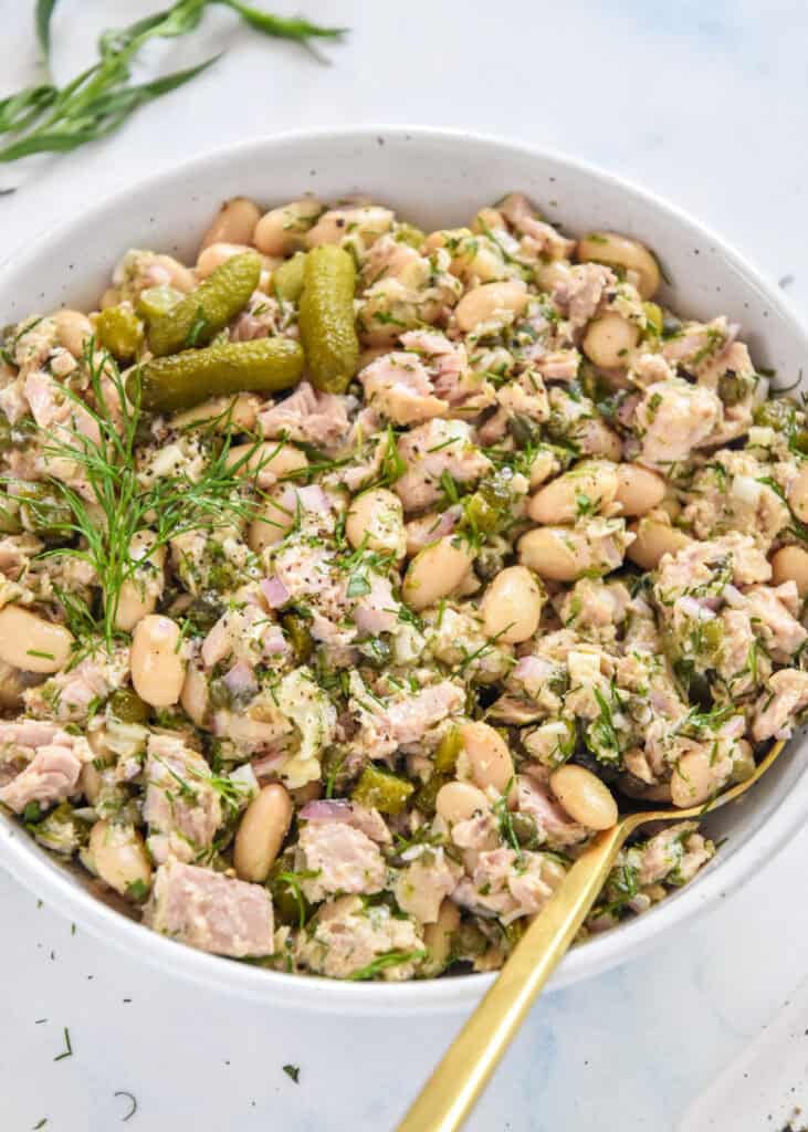 French-Style Tuna White Bean Salad in a bowl with fresh herbs, gherkins and a spoon in the bowl.