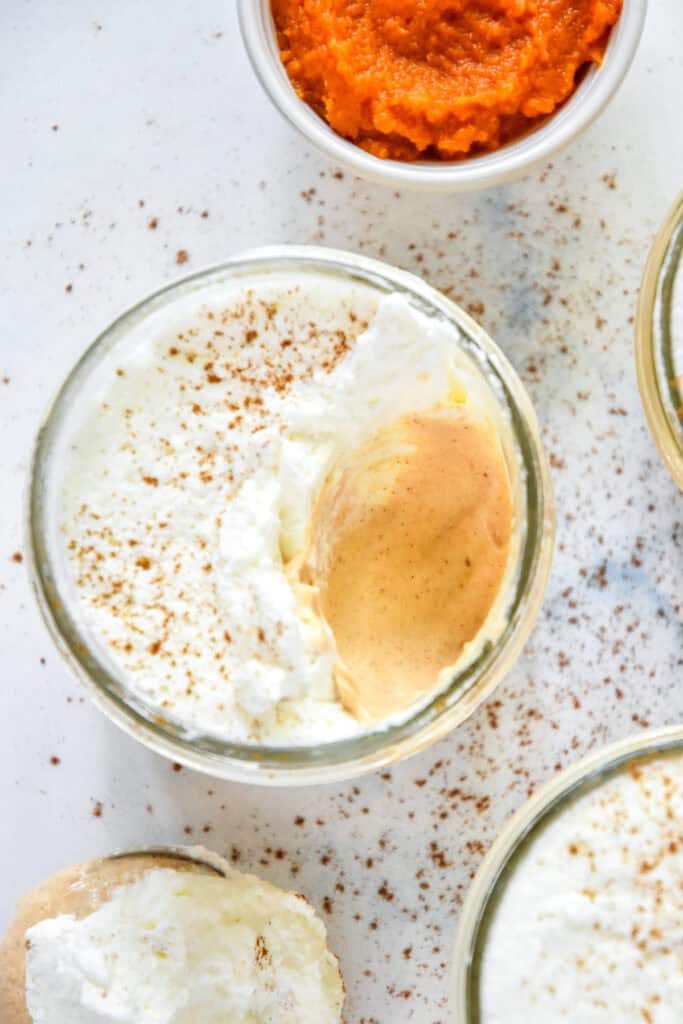 pumpkin spice whipped greek yogurt in individual mason jars with whipped cream and a bite taken out.