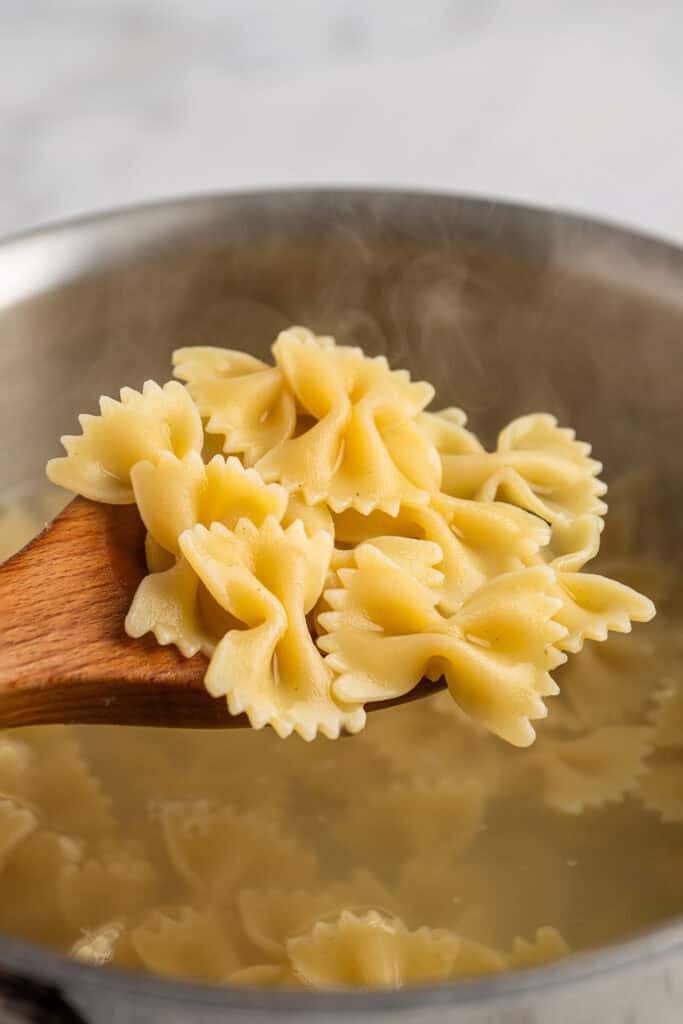 cooked bowtie pasta on a wooden spoon over pot of boiling water.